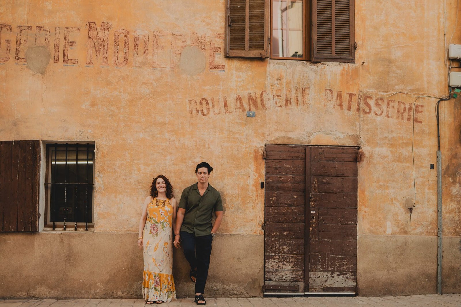 Couple posant dans une ruelle devant une façade patinée dans le centre de Cassis.